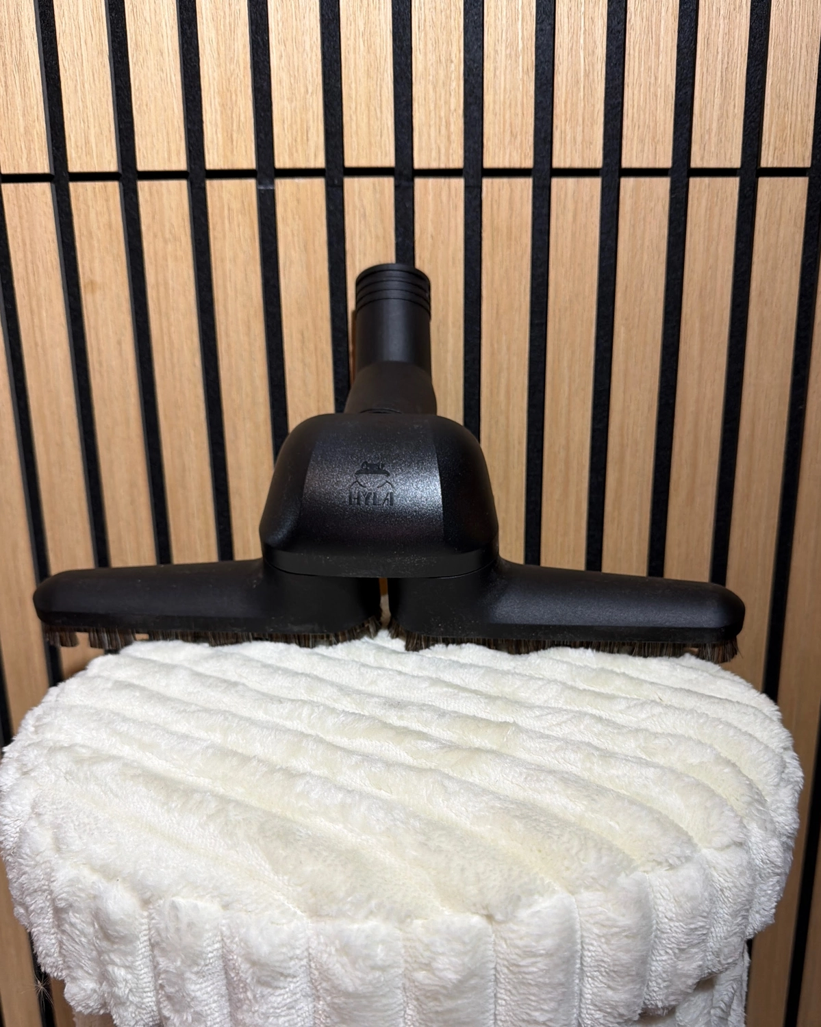 Black vacuum cleaner brush head with the brand name Hyla on a white textured microfiber cloth background.